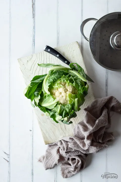 A whole cauliflower on a chopping board with a knife