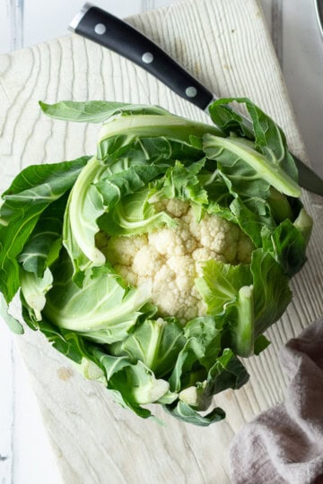 A whole cauliflower on a chopping board with a knife