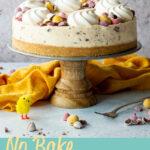 A Mini Egg cheesecake on a cake stand with a yellow chick and a fork at the side. A text overlay says 'no bake Mini Egg cheesecake'.