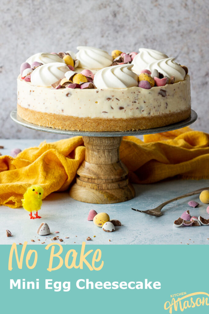 A Mini Egg cheesecake on a cake stand with a yellow chick and a fork at the side. A text overlay says 'no bake Mini Egg cheesecake'.