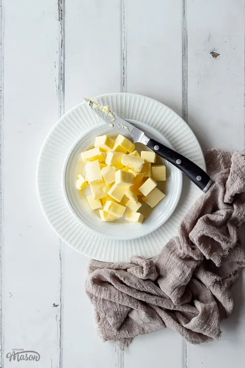 A plate of cubed butter with a sharp knife and a napkin