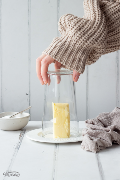 Someone placing a warm glass over a stick of butter on a plate