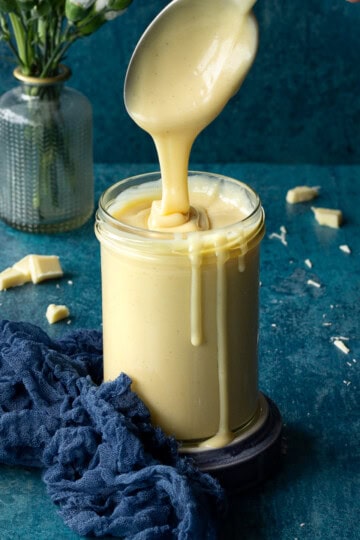 A spoon rippling white chocolate sauce in a glass jar