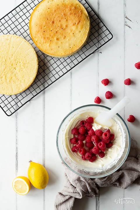 Raspberries being folded into icing and cake layers on a cooling rack