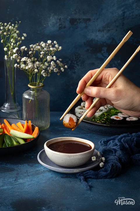 Sushi being dunked into sauce with chopsticks