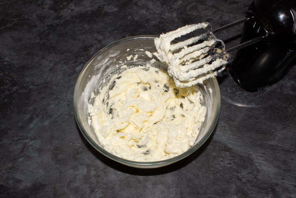 Creamed butter and icing sugar being whisked in a glass bowl