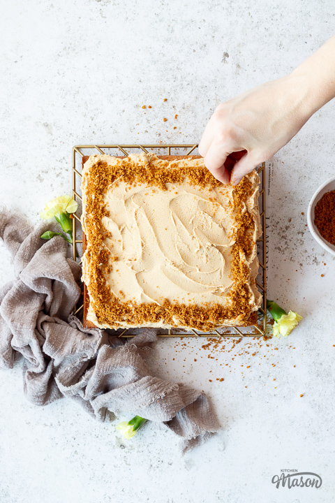 Biscuits crumbs being scattered over a Biscoff traybake