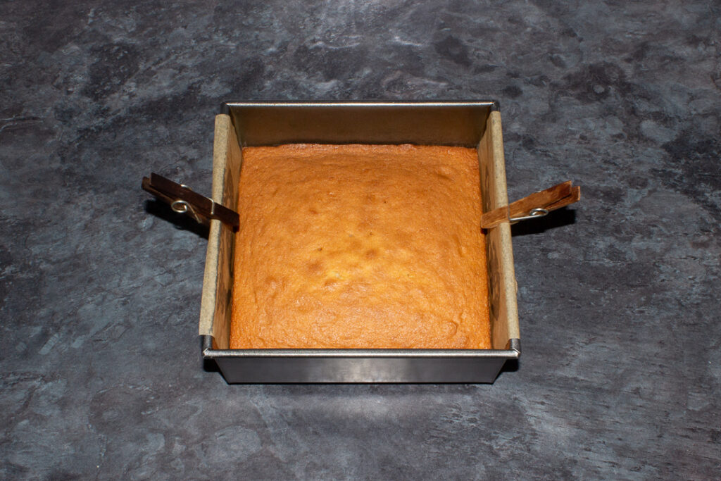 Baked sponge cake in a lined square tin.