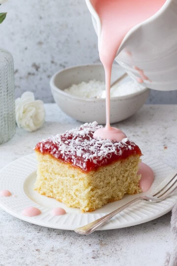 Custard being poured over a slice of coconut jam cake