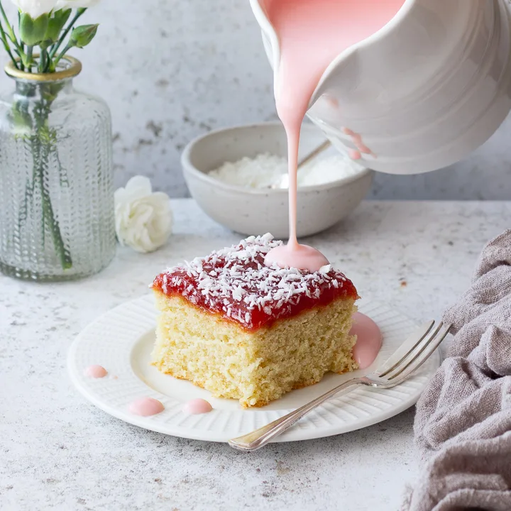 Custard being poured over a slice of coconut jam cake
