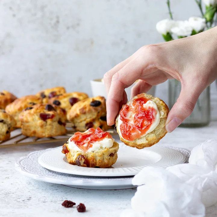 Someone picking up a fruit scone topped with jam and clotted cream.