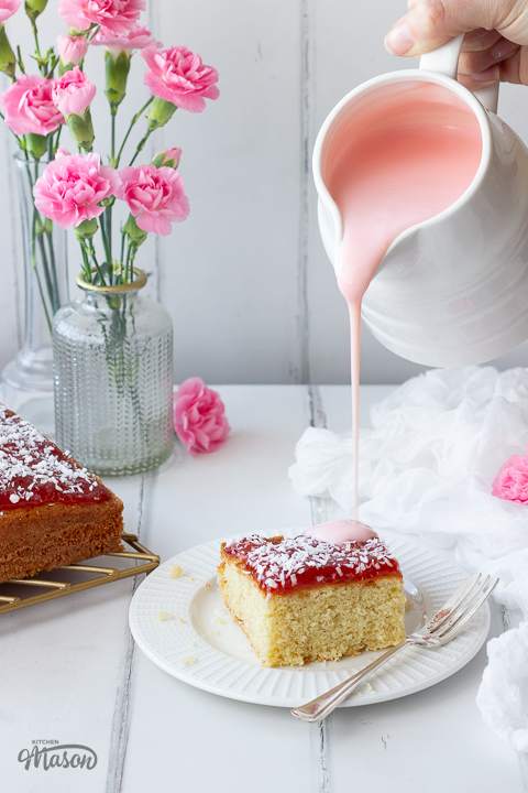 Pink custard being poured over coconut jam cake