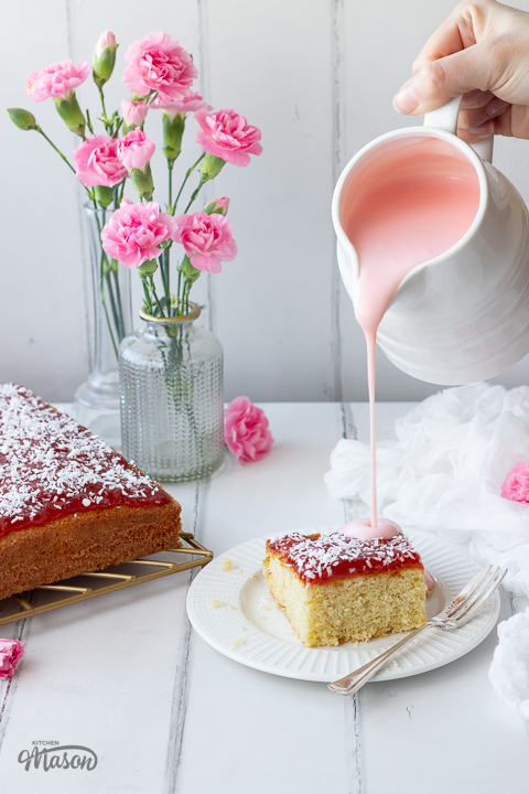 Pink custard being poured onto jam coconut sponge