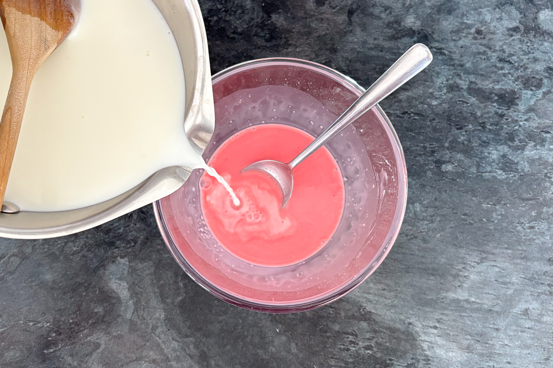 Hot milk being poured over strawberry blancmange paste