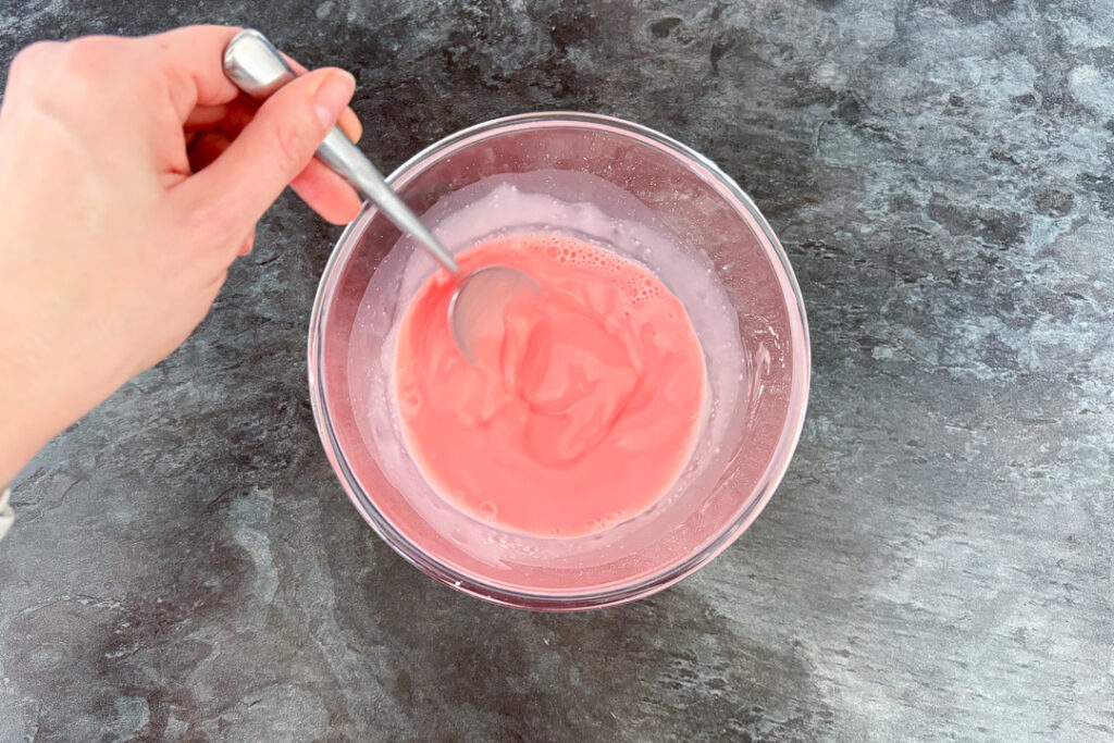 Hot milk being stirred into strawberry blancmange paste