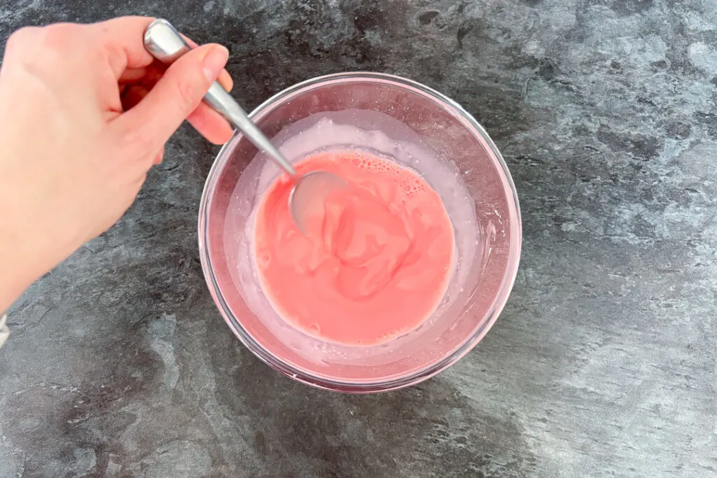 Hot milk being stirred into strawberry blancmange paste