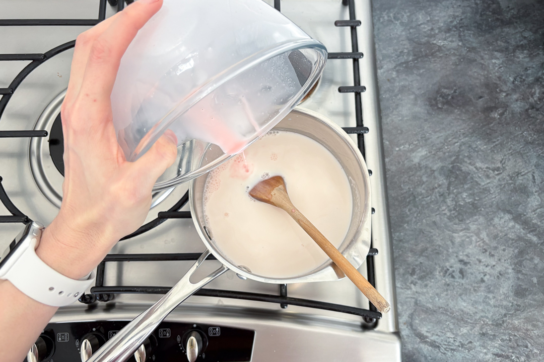 Blancmange paste being poured into hot milk in a saucepan