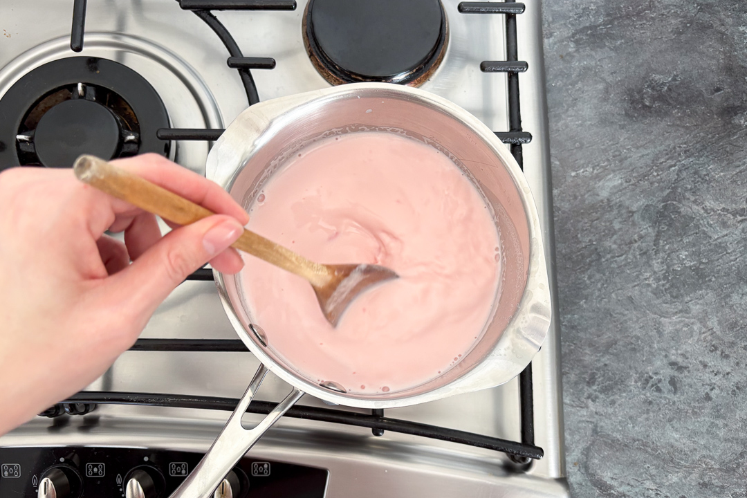 Pink custard being stirred in a saucepan