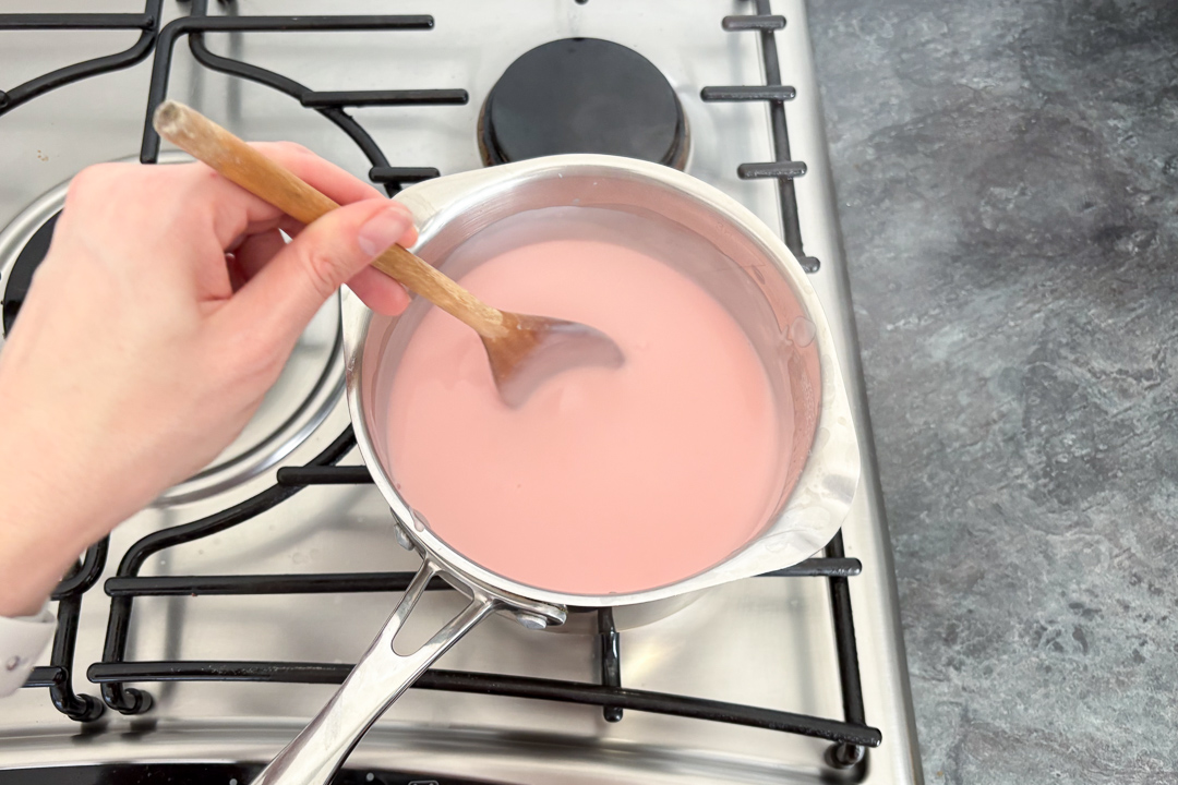Thick school pink custard in a saucepan with a spoon