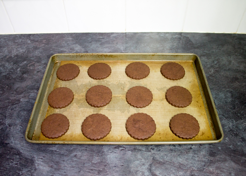 Baked chocolate biscuits on a lined baking tray.