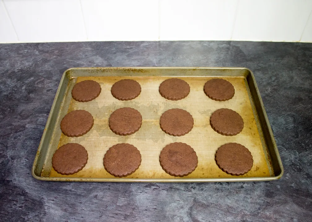Baked chocolate biscuits on a lined baking tray.