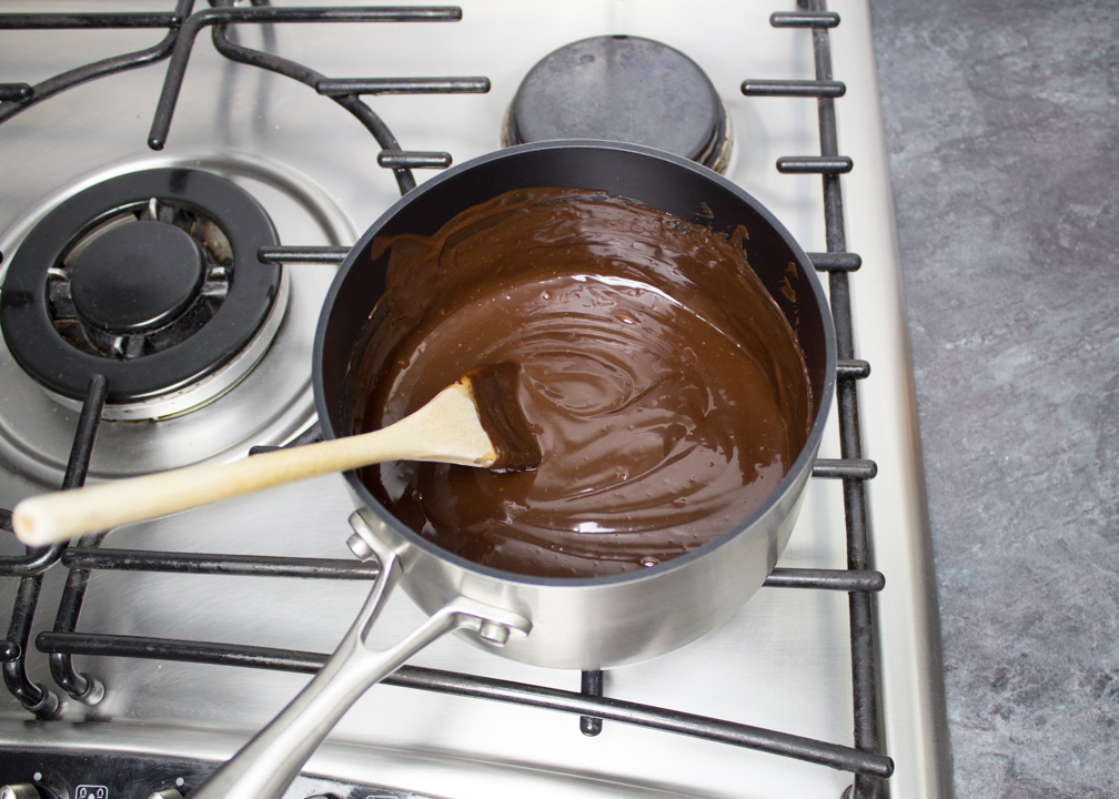 A warm chocolate sauce in a saucepan with a wooden spoon.