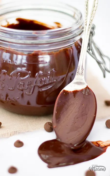 A spoon full of chocolate sauce dripping over a worktop.
