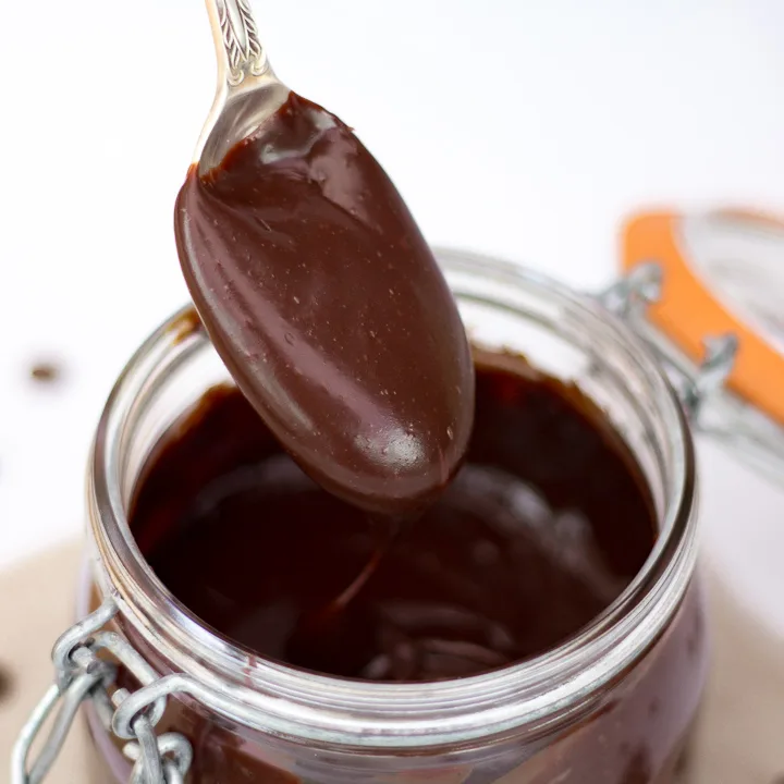 A thick and rich chocolate sauce being spooned from a jar.