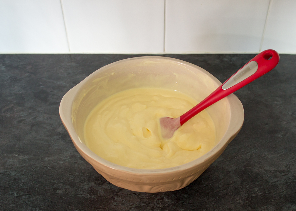 Melting vanilla ice cream in a large mixing bowl with a spatula.