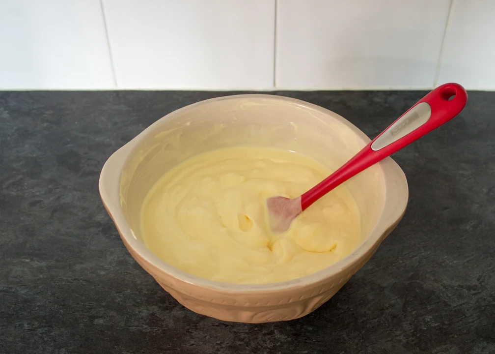 Melting vanilla ice cream in a large mixing bowl with a spatula.