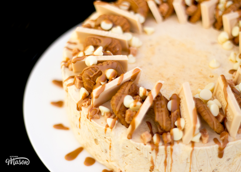 A fully decorated Biscoff ice cream cake on a white place. The top has been drizzled with melted Biscoff spread.