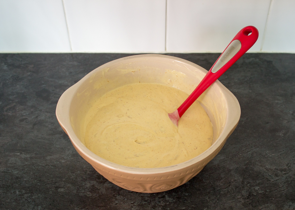 Biscoff flavoured ice cream in a large mixing bowl with a spatula.