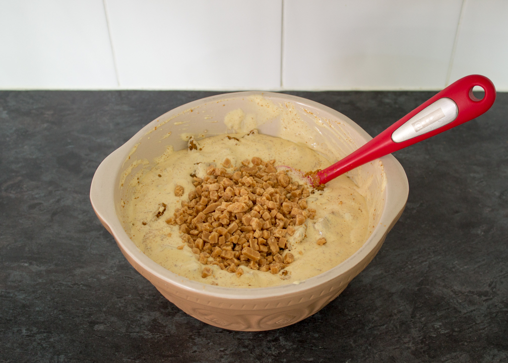 Small fudge pieces being mixed into melted ice cream.