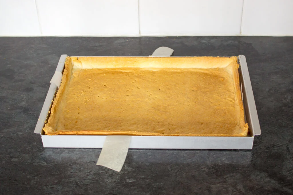 A baking tin lined with baked shortcrust pastry, with the edges neatly trimmed.