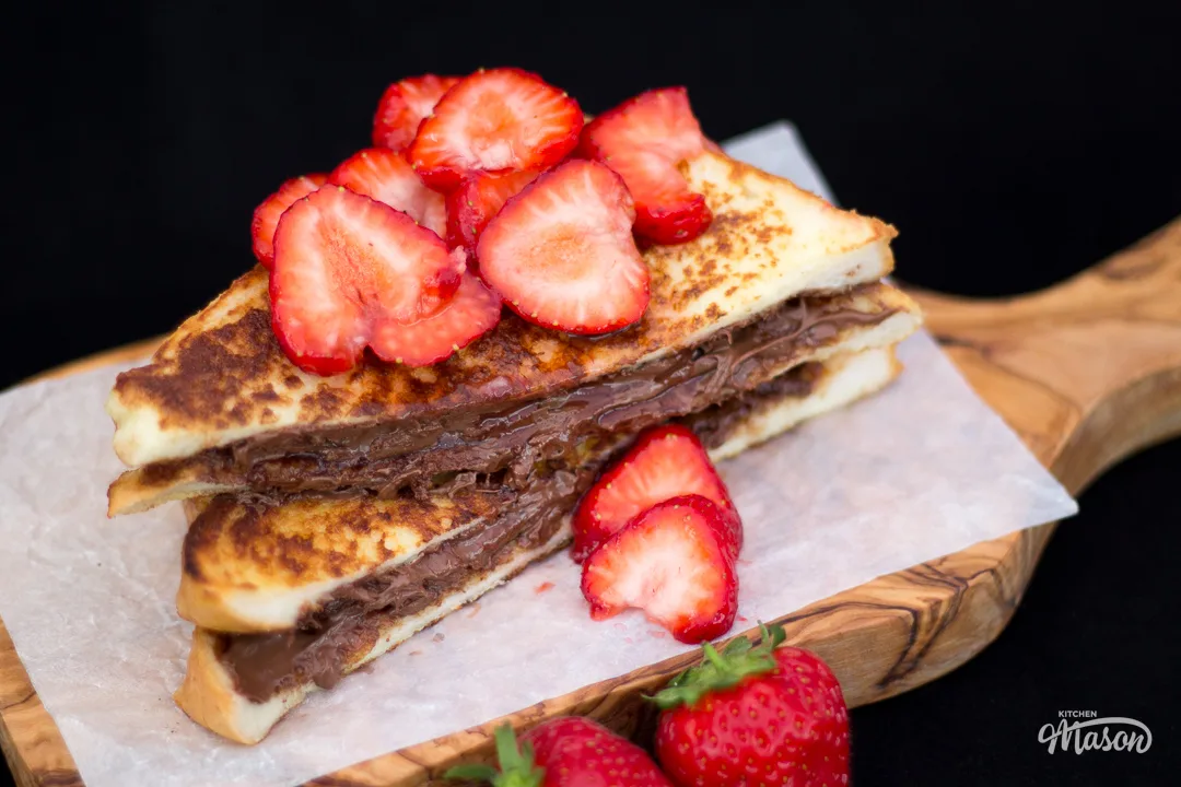 Strawberry Nutella French toast sliced in half on a chopping board.
