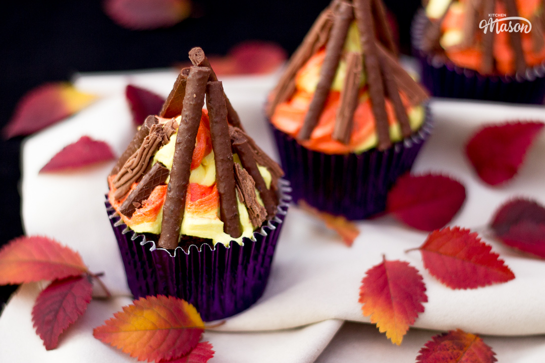 Three bonfire cupcakes in purple cupcake cases, with red and orange leaves scattered around them.