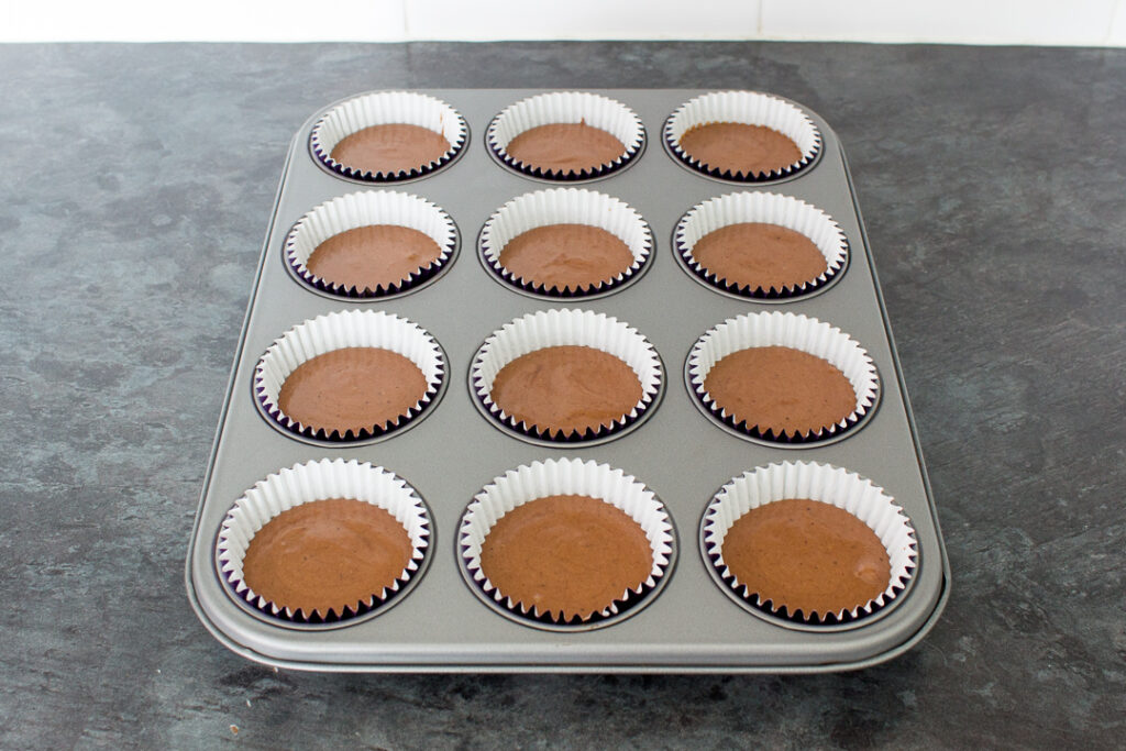Chocolate cupcake batter in cases set in a cupcake tin, ready to be baked in the oven.