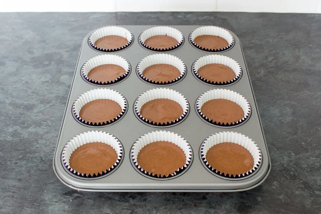 Chocolate cupcake batter in cases set in a cupcake tin, ready to be baked in the oven.