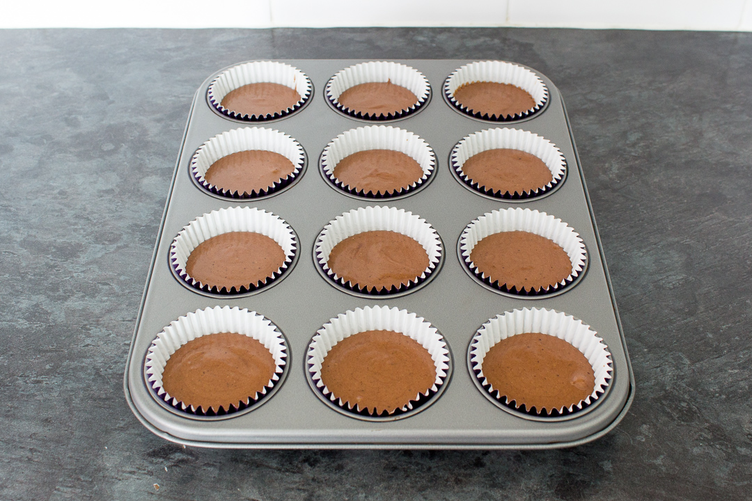 Chocolate cupcake batter in cases set in a cupcake tin, ready to be baked in the oven.