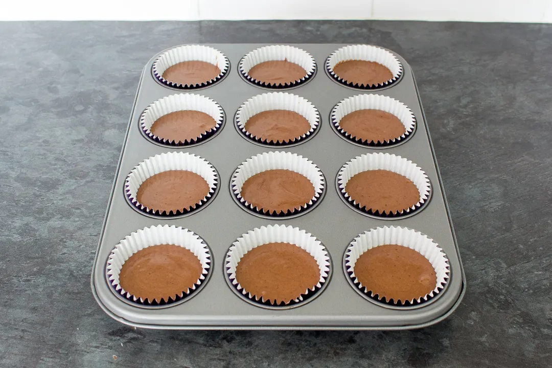 Chocolate cupcake batter in cases set in a cupcake tin, ready to be baked in the oven.