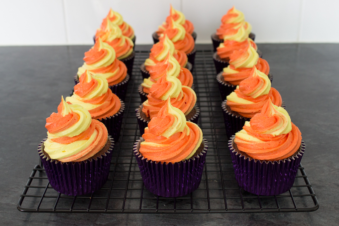 Chocolate cupcakes topped with large swirls of orange and yellow buttercream frosting.