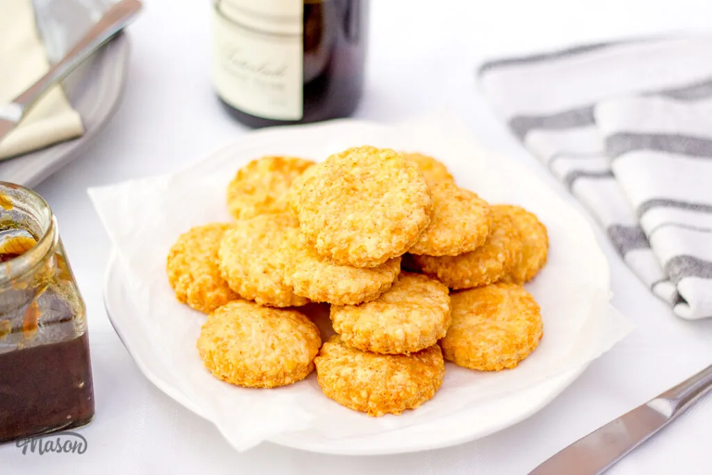Cheese biscuits stacked up on a white plate with a jar of chutney at the side.