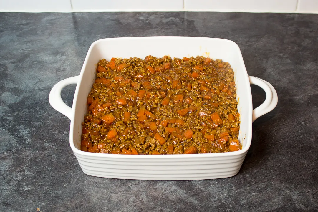 Cooked vegetables and mince in a square white dish.