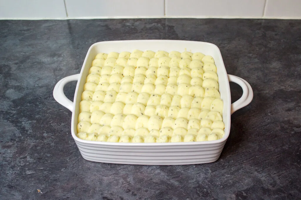 Mashed potatoes piped over the top of mince and vegetables in a white square dish.