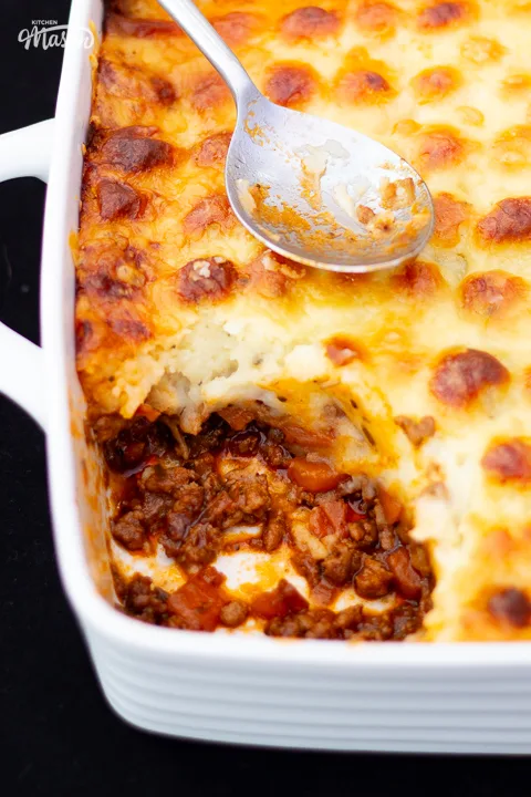 Cooked shepherd's pie in a white dish with a portion spooned out.