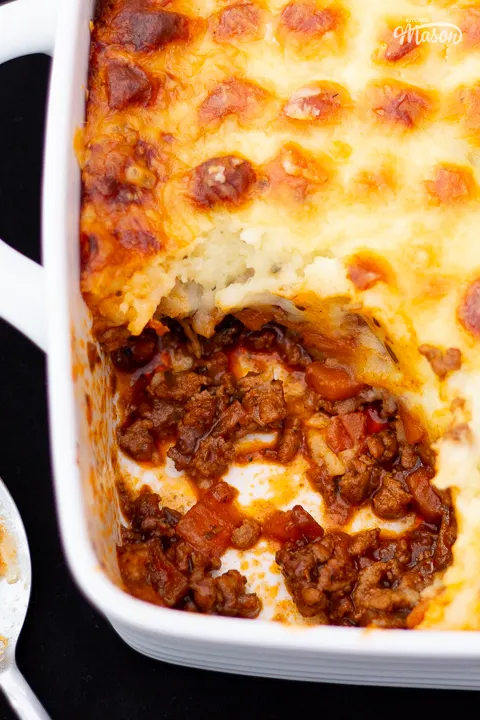 Baked Shepherd's pie in a white dish with a portion spooned out, and a spoon on the side.
