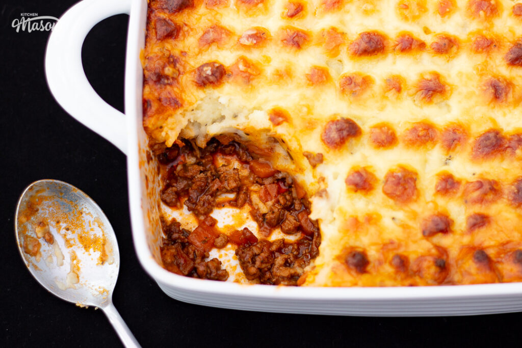 Shepherd's pie in a square white roasting dish with a dirty spoon at the side, and a portion spooned out.