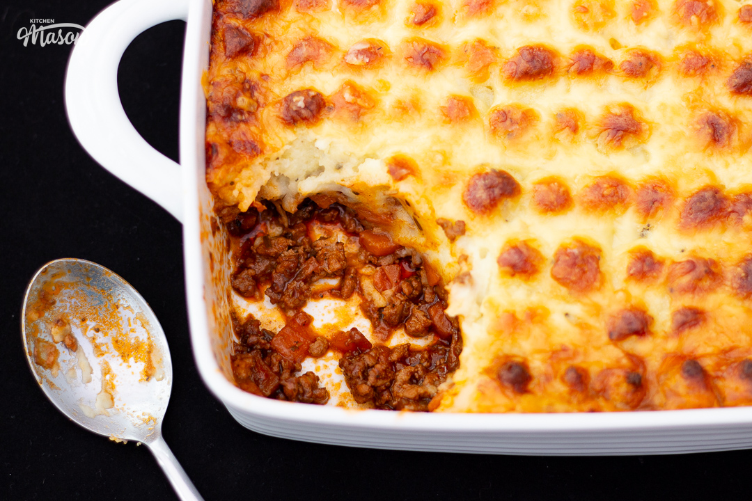 Shepherd's pie in a square white roasting dish with a dirty spoon at the side, and a portion spooned out.
