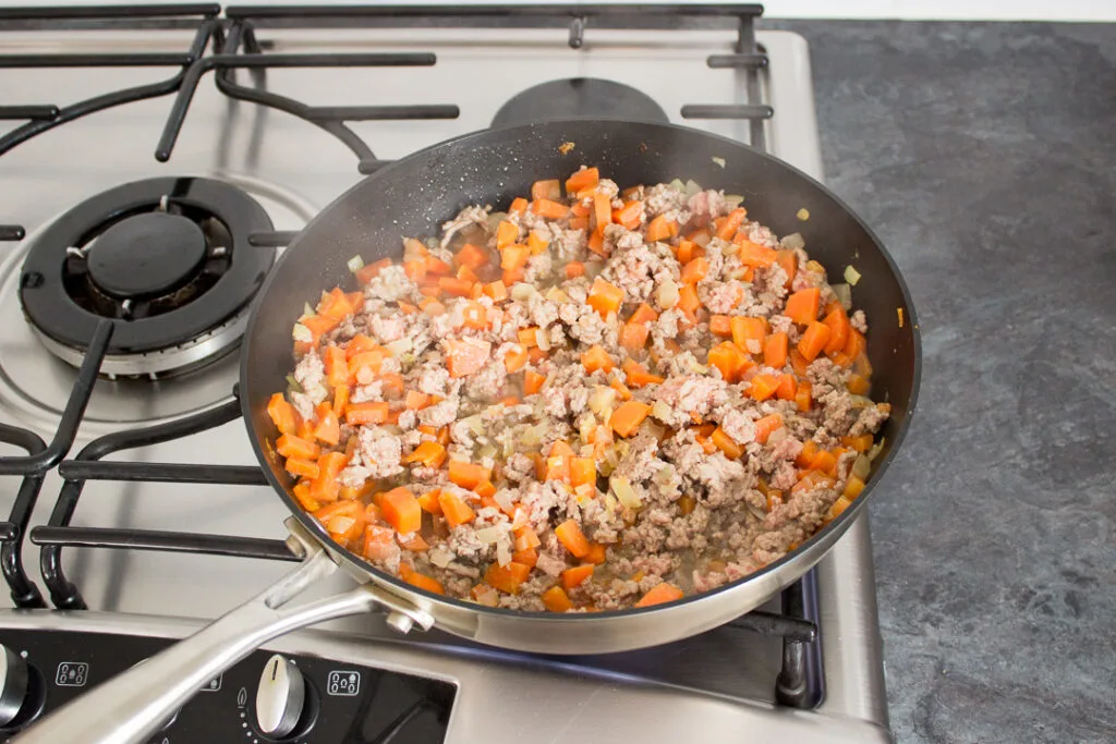 Root vegetables and mince cooking in a large frying pan.