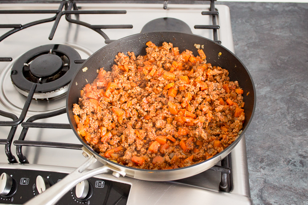 Mince, vegetables, sauces and seasonings cooking in a large frying pan.